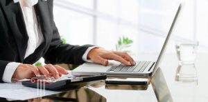 Woman working on tax documents at desk with computer and calculator.