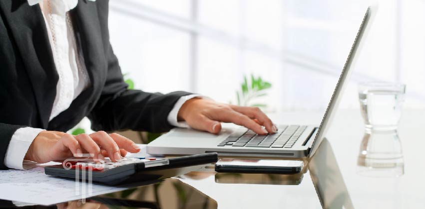 Woman working on tax documents at desk with computer and calculator.